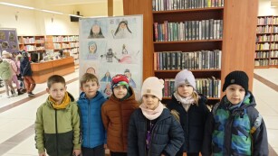 dzieci pozują do zdjęcia na tle sztalug z pracami plastycznymi w bibliotece