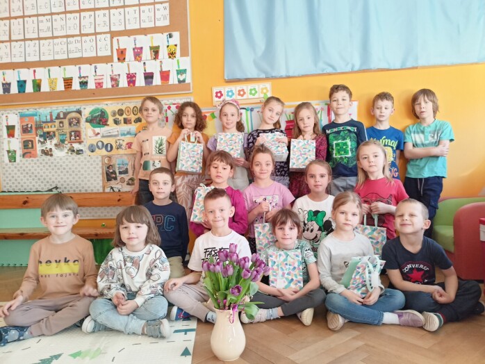 dzieci pozują do zdjęcia z prezentami w rękach, na podłodze stoi flakon z tulipanami