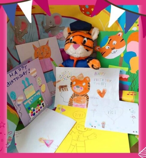 pluszowy tygrys na kolorowym tle, wokół niego kartki urodzinowe wykonane przez dzieci