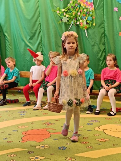dziewczynka w stroju wiosny, z koszykiem, w tle inne dzieci w wiosennych strojach, na zielonym tle