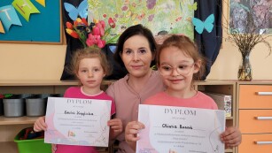 nauczycielka i dwie dziewczynki pozują do zdjęcia z dyplomami