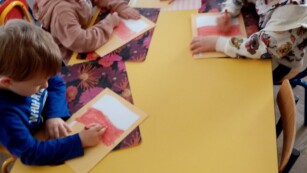 kilkoro dzieci siedzi przy stole, rysują i kolorują flagi Polski